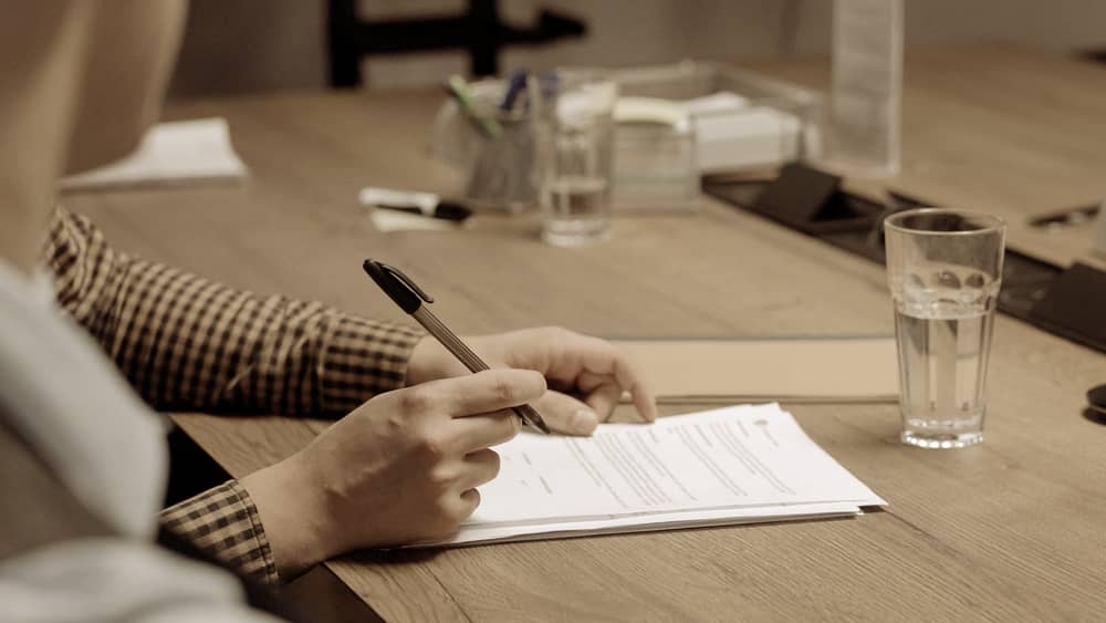 Hands signing printed documents at a desk